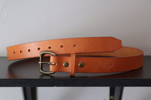 Tan leather belt with brass buckle on wood in front of American flag