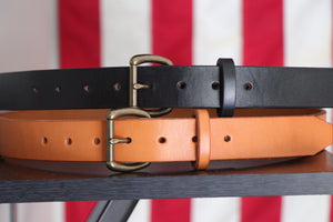 Black and Russet leather belts with brass buckles on wood in front of American flag