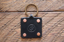 Black handmade leather key fob with brass keyring and copper rivets on wood
