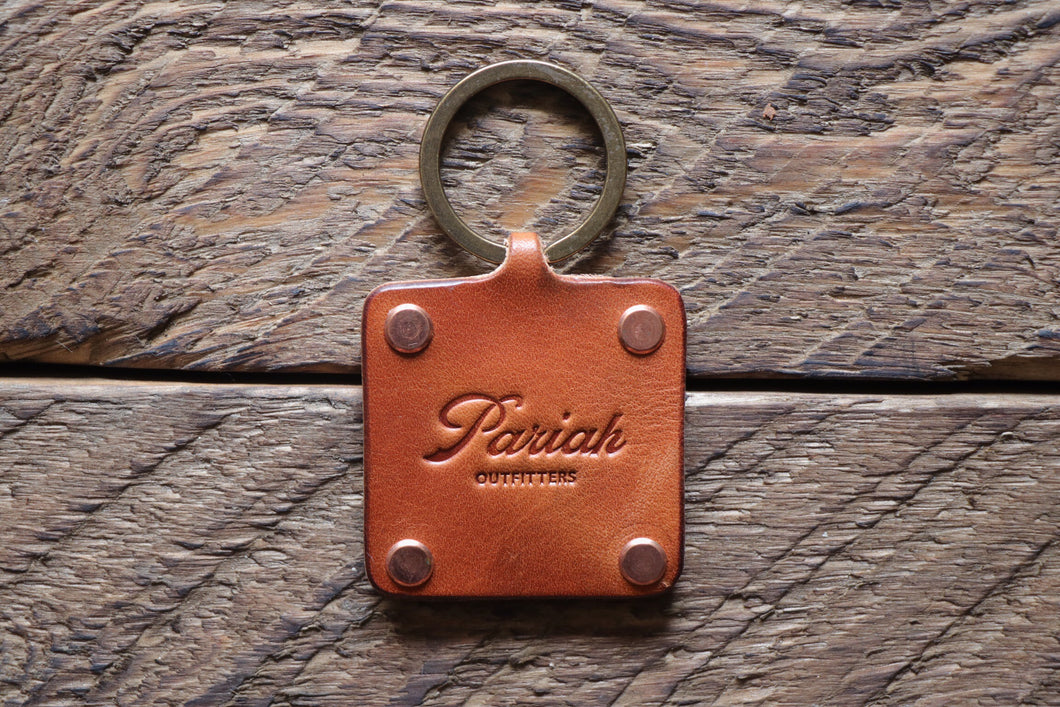 Brown handmade leather key fob with brass keyring and copper rivets on wood
