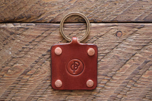 Brown handmade leather key fob with brass keyring and copper rivets on wood